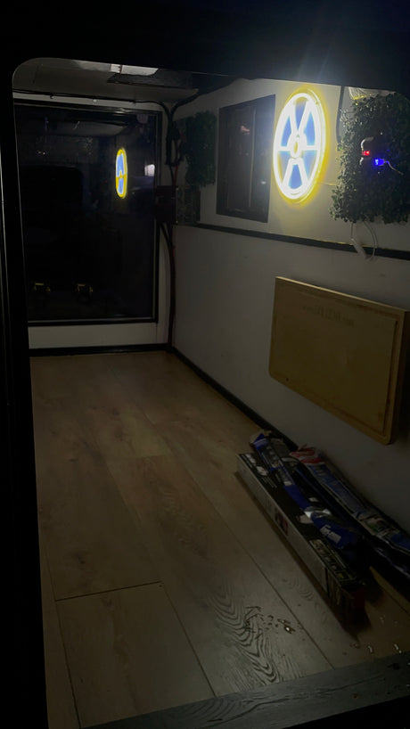 RV rental's cozy interior showcases wooden flooring, a unique glowing neon sign, and practical storage boxes.