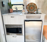 Compact and cozy RV rental kitchen with sink, microwave, refrigerator, and scenic views, ideal for travel.