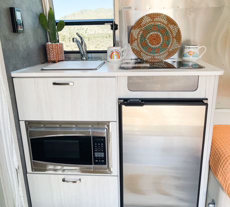 Compact and cozy RV rental kitchen with sink, microwave, refrigerator, and scenic views, ideal for travel.