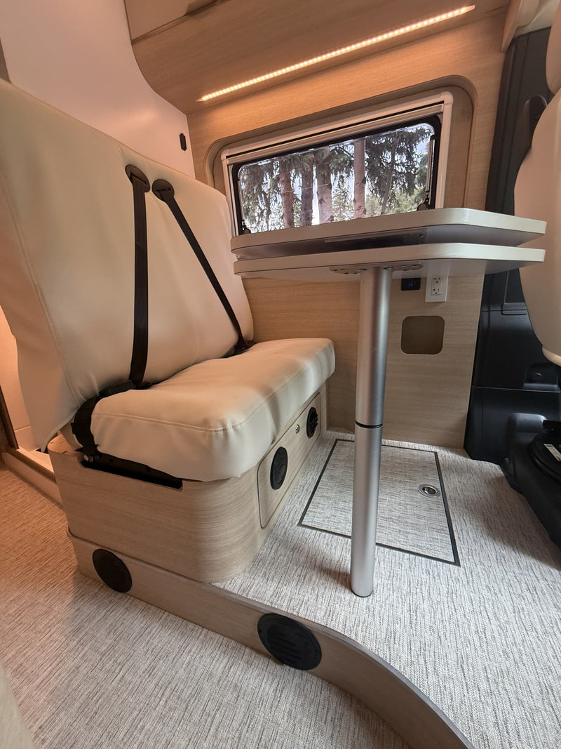 Modern RV rental interior: cream bench seat with belts, adjustable table, window with tree view, and ambient lighting. — photo 10