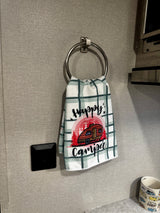 Inside an RV rental: A plaid "Happy Camper" towel hangs by a control panel and countertop mug.