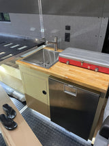 This RV rental kitchenette features a stainless sink, portable stove, Dometic fridge, and a functional wooden countertop.