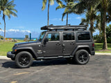Dark gray Jeep Wrangler Unlimited with rooftop tent, parked at a tropical beach—ideal for your next RV rental adventure.