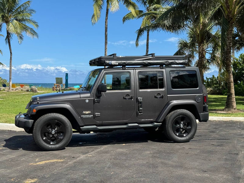 Dark gray Jeep Wrangler Unlimited with rooftop tent, parked at a tropical beach—ideal for your next RV rental adventure. — photo 11