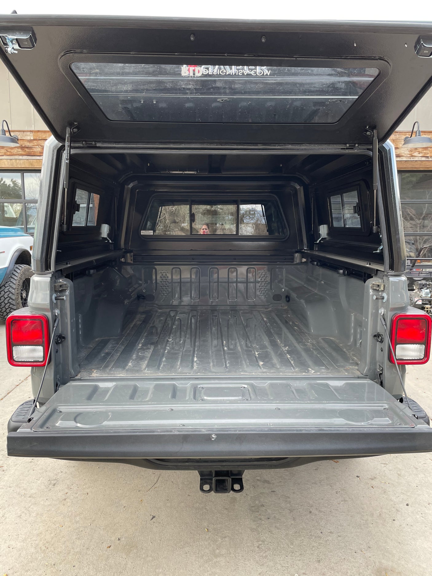 Grey pickup truck with open tailgate and black camper shell raised, revealing an empty bed; ideal for an RV rental.