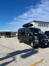 Black RV rental van with roof box parked at Edisto Watersports, near bike rentals. Ready for outdoor adventures.