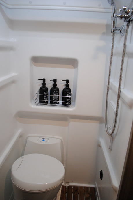 Step inside this compact RV rental bathroom, featuring a modern toilet, a refreshing shower, and organized amenities for your comfort.