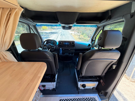 RV rental camper van interior. View from living area to front cockpit with dashboard, steering wheel, seats & wooden ceiling.