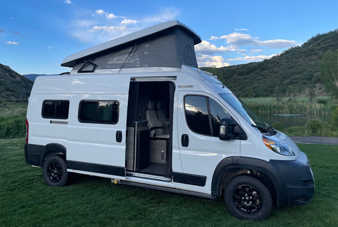 White pop-top camper van parked in a scenic mountain setting, ready for your next rv rental adventure. Interior visible through open door.