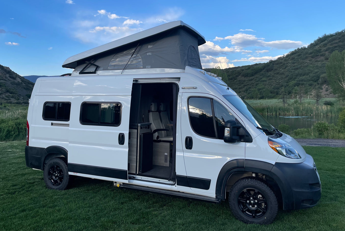 White pop-top camper van parked in a scenic mountain setting, ready for your next rv rental adventure. Interior visible through open door.