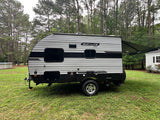A grey and black striped Sun Lite Sport RV rental, a travel trailer with an extended awning, parked on green grass near trees.