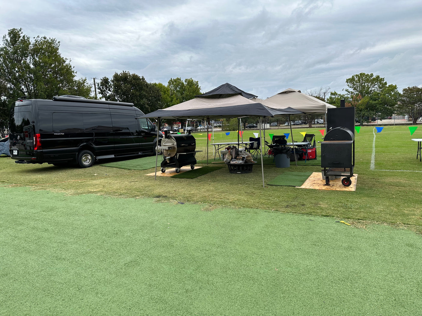 Luxury black van setup with tents, smokers, and outdoor seating on a green field, perfect for an RV rental tailgate event.