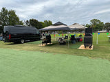 Luxury black van setup with tents, smokers, and outdoor seating on a green field, perfect for an RV rental tailgate event.