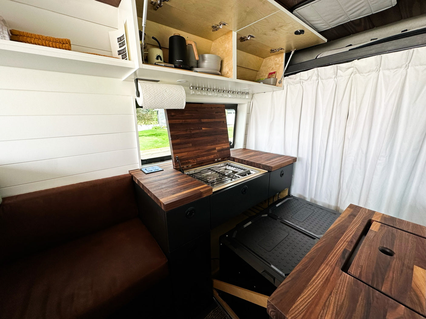 RV rental: Modern camper van kitchen w/ wood counters, built-in stove, overhead storage & comfy seating.
