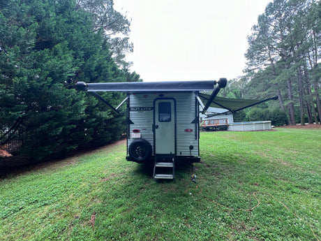 RV rental: A light grey Sun Lite Sport travel trailer with an extended awning, parked on a green lawn ready for camping.