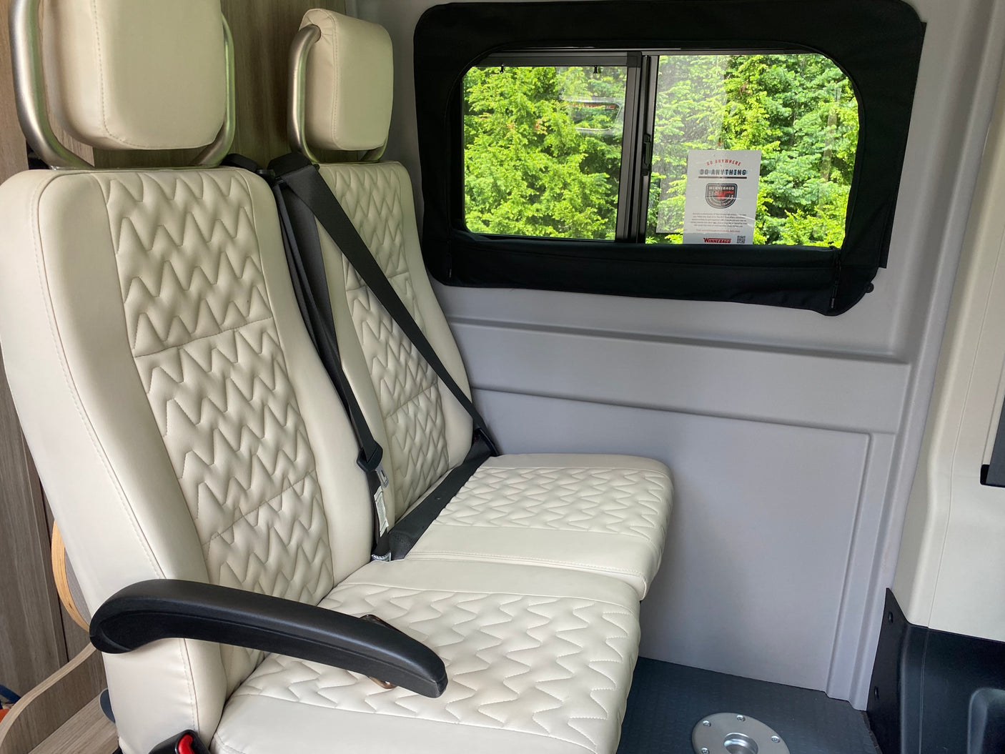 Interior of an RV rental showcasing comfortable, beige quilted seats with seatbelts, and a window view of lush trees.