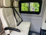Interior of an RV rental showcasing comfortable, beige quilted seats with seatbelts, and a window view of lush trees.