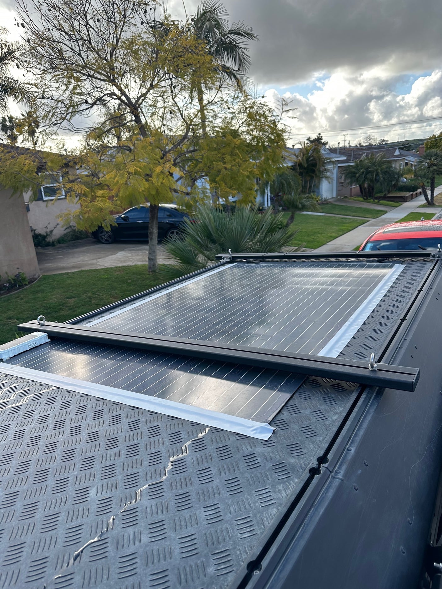 Solar panels on an RV rental roof, featuring diamond plate texture, overlooking a street and cloudy sky.
