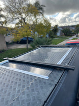 Solar panels on an RV rental roof, featuring diamond plate texture, overlooking a street and cloudy sky.