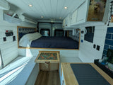Cozy RV rental interior with a full bed, convertible table, compact kitchen, and white shiplap walls for comfy travel.