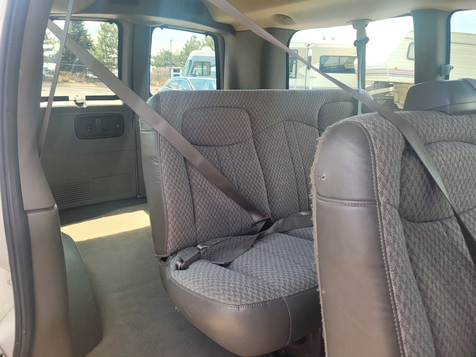 Inside a vehicle, showing back passenger seats and seatbelts. RVs seen outside, perhaps at an RV rental lot.