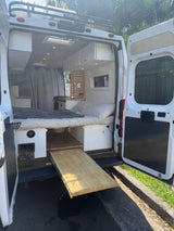 RV rental: Inside a modern camper van showing a cozy bed, pull-out table, kitchenette, and overhead storage, ready for adventure.