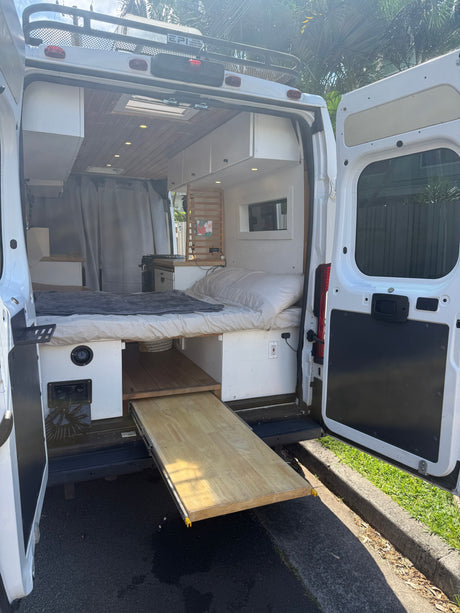 RV rental: Inside a modern camper van showing a cozy bed, pull-out table, kitchenette, and overhead storage, ready for adventure.
