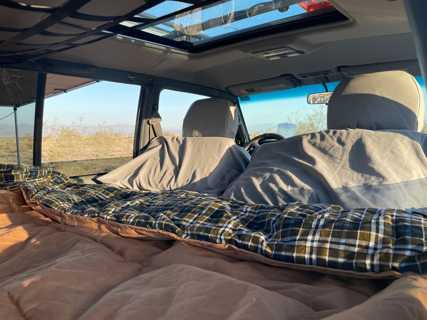 Vehicle interior with cozy plaid bedding for sleeping, open sunroof, and scenic desert views, ideal for an rv rental road trip. — photo 2