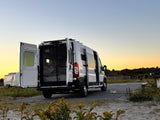 This rv rental campervan, doors open, shows its cozy interior at sunset. Parked by the beach for van life travel.