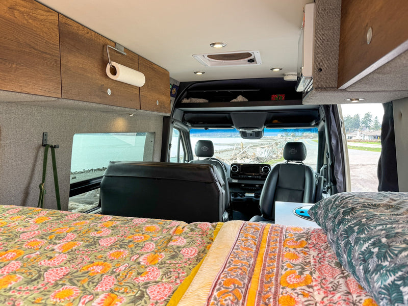 RV rental: Inside a camper van featuring a vibrant bed, overhead cabinets, and front cockpit with scenic views. — photo 9