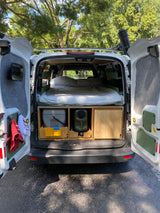 This cozy camper van conversion, perfect for an RV rental, shows its bed, toilet, and water setup, ready for adventure.