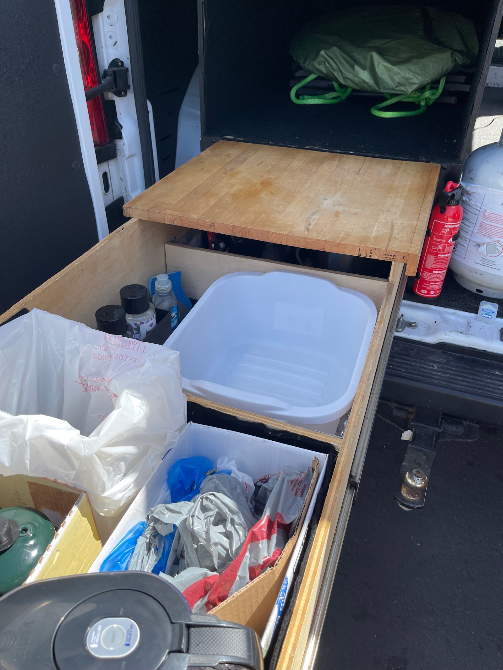 Organized rv rental pull-out kitchen/storage in a van: basin, cutting board, fire extinguisher, cleaning supplies, & camping gear.
