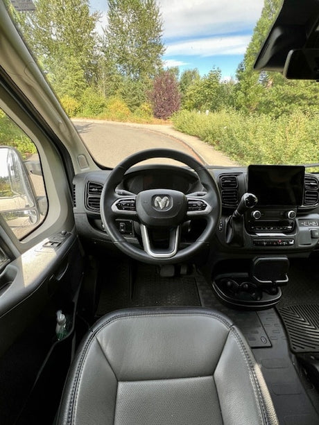 Driver's view of a spacious RV rental interior: Ram steering wheel, dash, and winding road ahead.