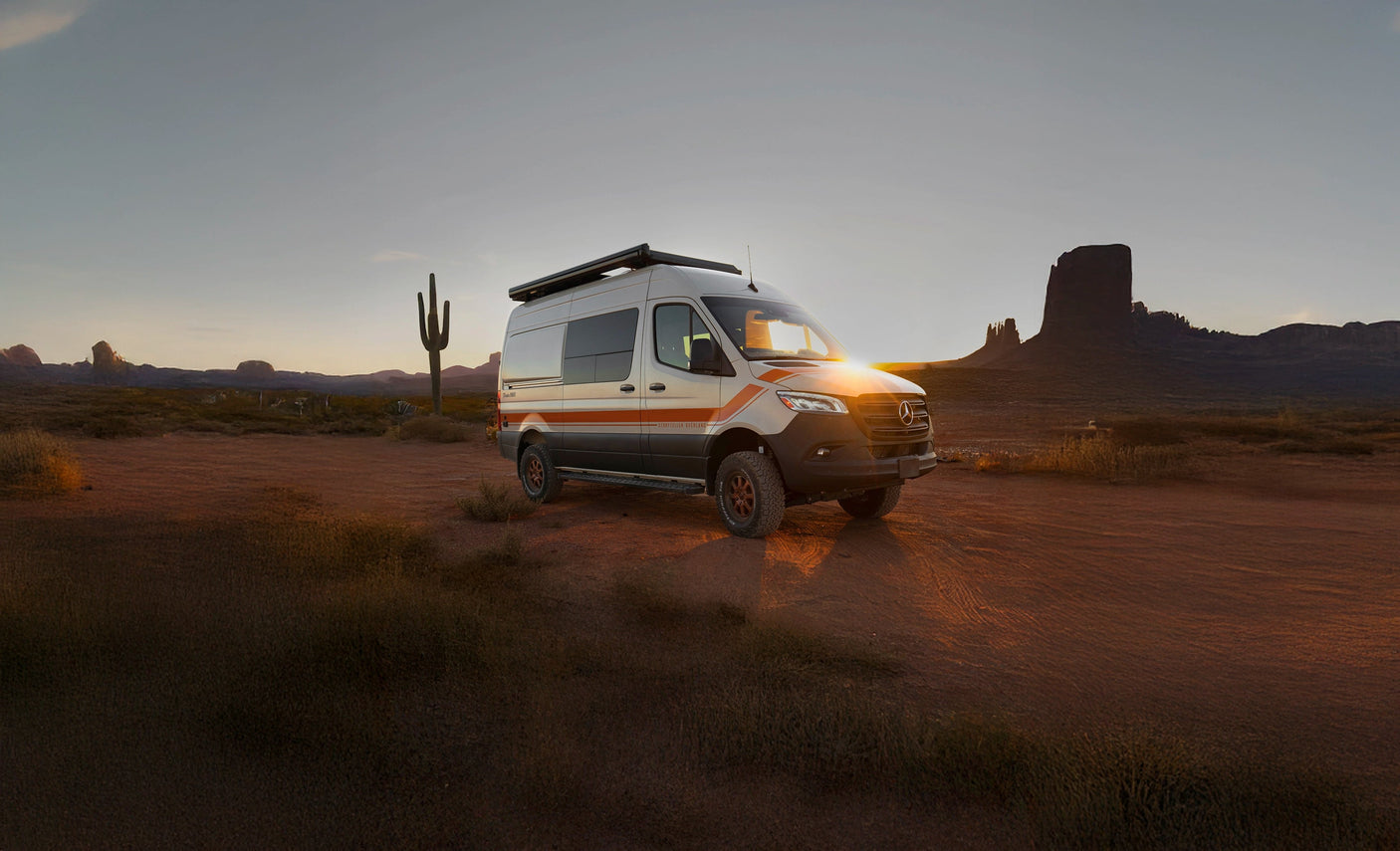 This white RV rental camper van, illuminated by the sunset in a sweeping desert landscape, awaits your adventure travel.
