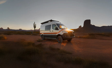 This white RV rental camper van, illuminated by the sunset in a sweeping desert landscape, awaits your adventure travel.