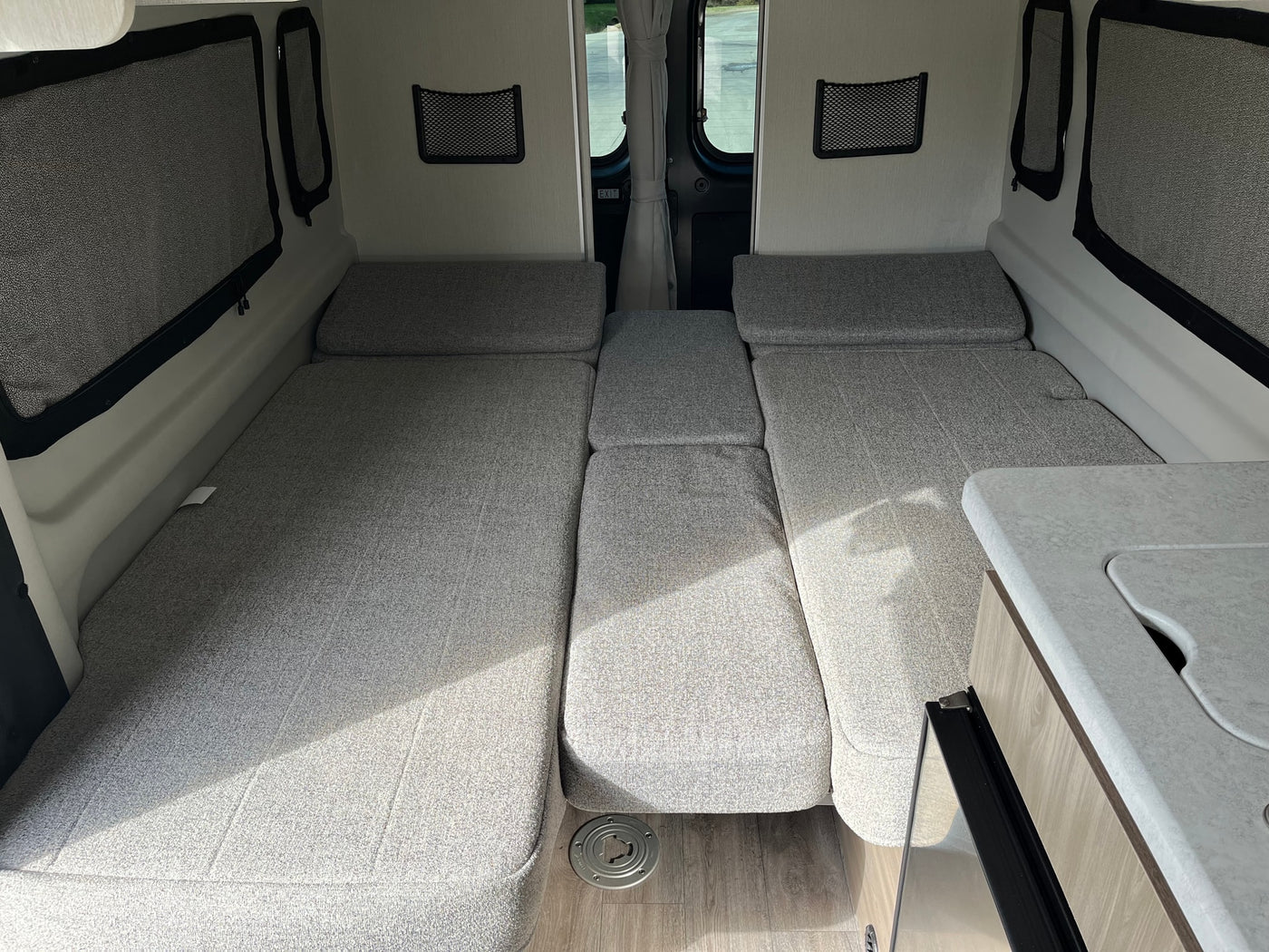 Light grey convertible beds and seating in a clean RV rental interior, showing a compact living area and small kitchen counter. — photo 20