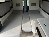 Light grey convertible beds and seating in a clean RV rental interior, showing a compact living area and small kitchen counter.