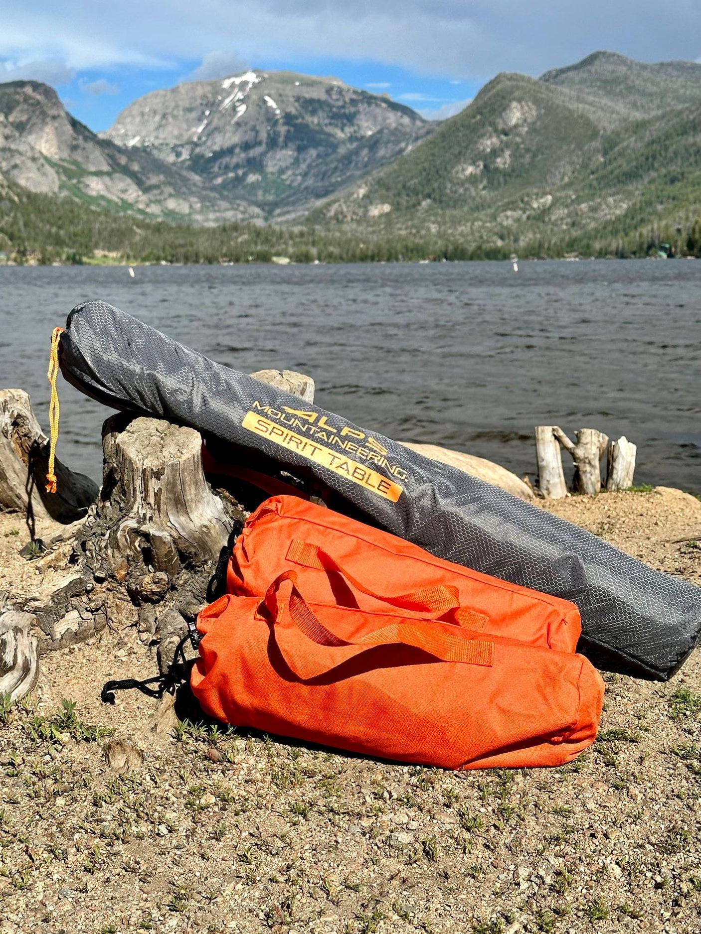 RV rental adventure: ALPS Mountaineering Spirit Table & gear by a scenic mountain lake with mountains in background.