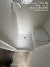 Compact RV rental bathroom: features a modern toilet and integrated shower pan with drain. Clean & functional.