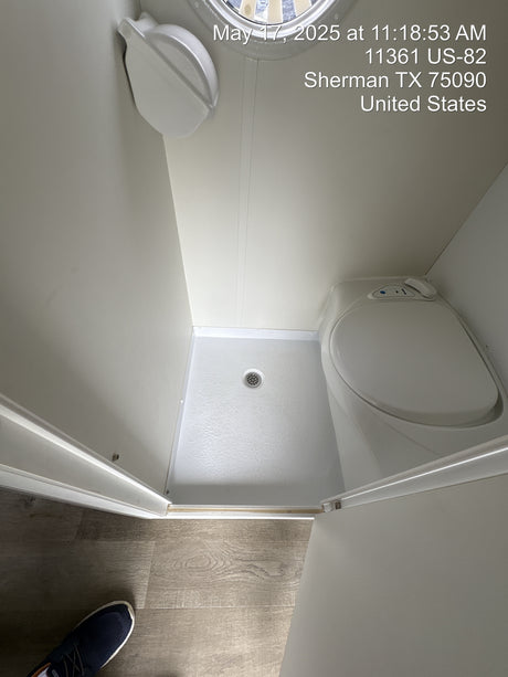 Compact RV rental bathroom: features a modern toilet and integrated shower pan with drain. Clean & functional.