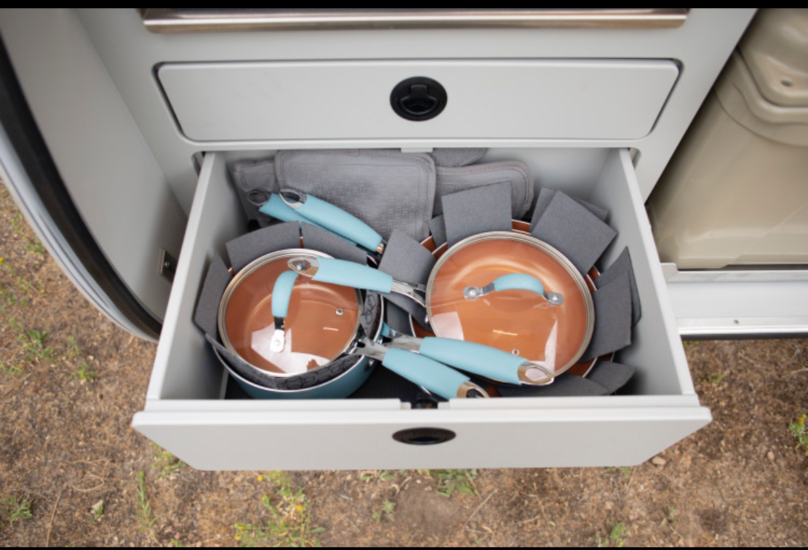 RV rental's kitchen drawer with organized blue-handled pots, pans, & gray protective pads for camping.