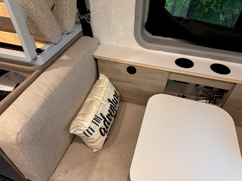  and essential water system controls. Ready for adventure.|White Ram ProMaster RV rental parked roadside with its side door open.|Cozy RV rental interior with convertible seating — photo 17