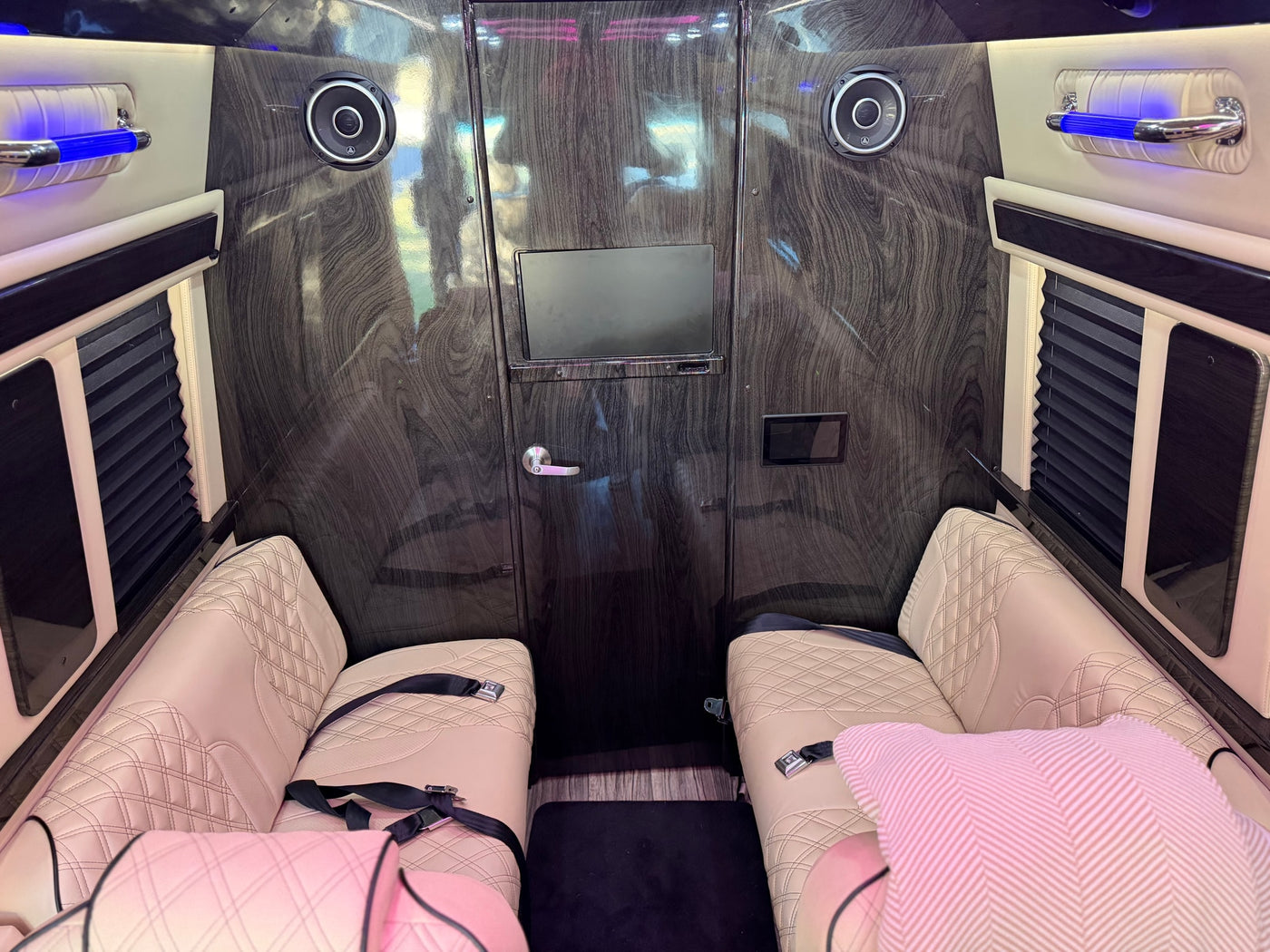 Explore this luxury RV rental: plush quilted seating, dark wood-grain interior, TV, premium audio, and blue ambient lighting. — photo 10