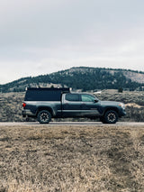 A dark grey Toyota Tacoma pickup with a truck camper, offering a compact rv rental option for exploring rugged terrain.