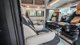 Interior of an rv rental with comfortable tan and black swivel seats, a small table, and overhead storage.