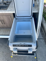 An open portable cooler/refrigerator on a slide-out tray, part of an RV rental kitchen setup with a sink.