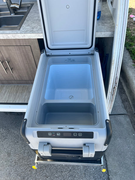An open portable cooler/refrigerator on a slide-out tray, part of an RV rental kitchen setup with a sink.
