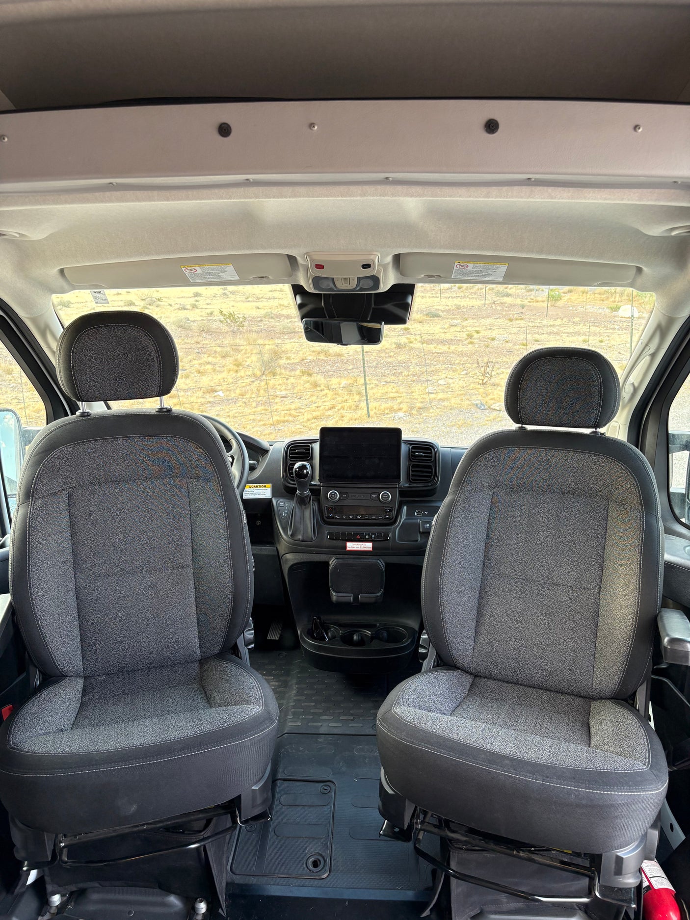 Inside an RV rental: spacious and clean front cabin with driver and passenger seats, modern dashboard, and open road view.