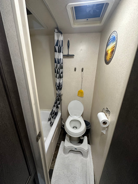 Functional RV rental bathroom: toilet, shower with patterned curtain, and ceiling vent. Compact & travel-ready.