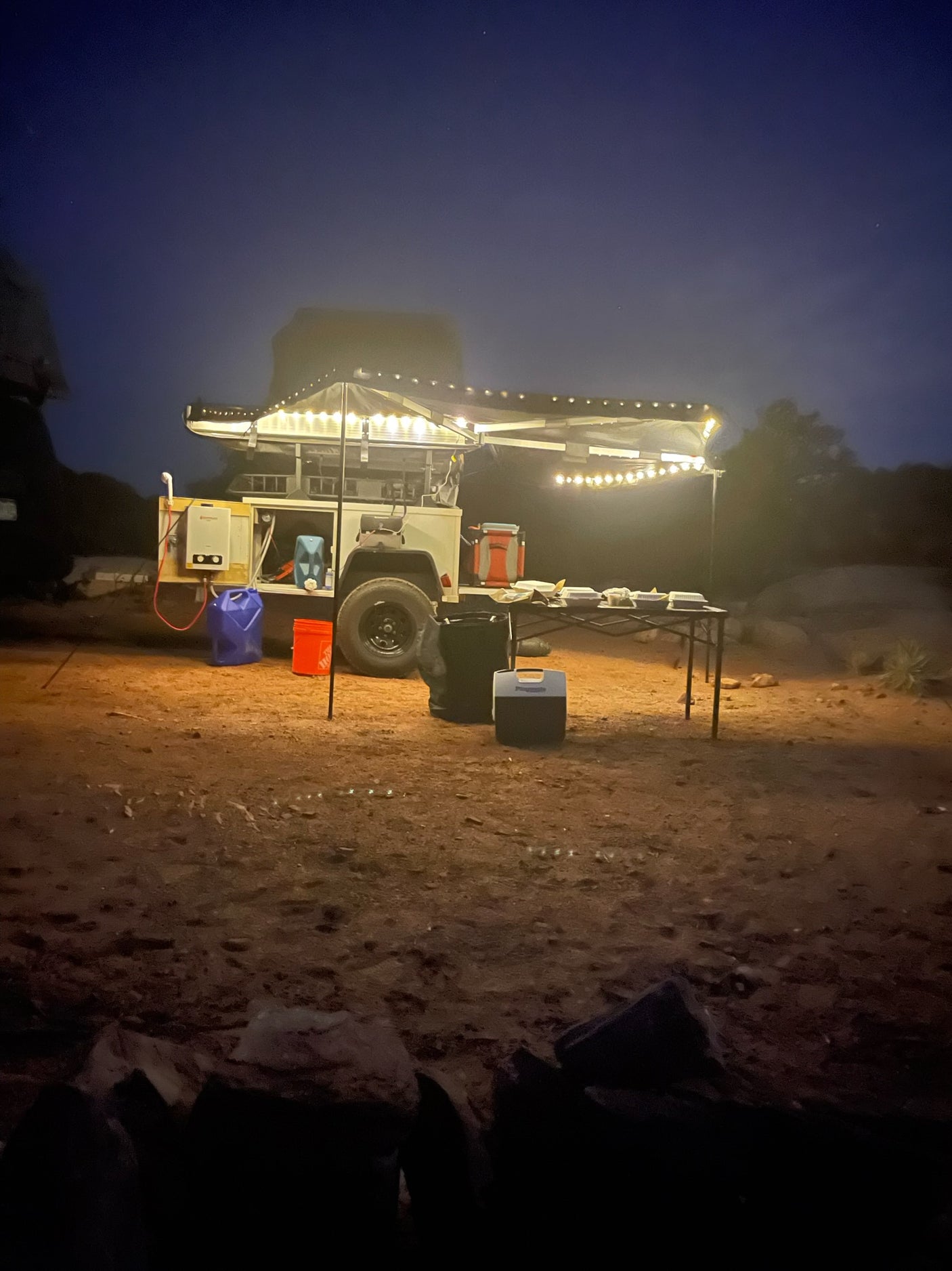 Nighttime off-grid desert camping with an RV rental. An illuminated overland trailer setup provides a cozy, comfortable mobile camp experience.